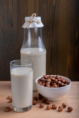 Glass of Hazelnut milk and bottle and organic hazelnuts on wooden background, Alternative Milk. Nuts milk