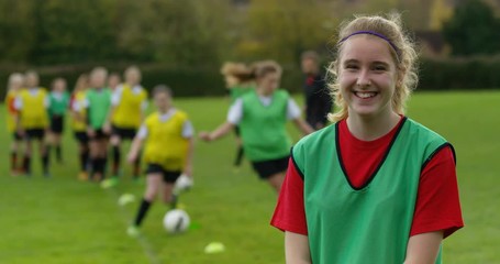4K Portrait smiling girl, youth soccer player with teammates training in background