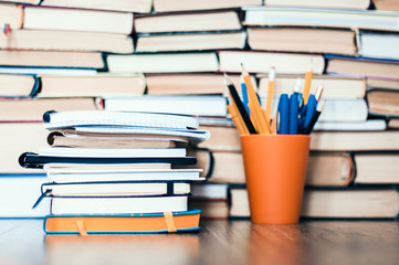 Stack of books, notebooks and pencils in plastic holder on wooden table with copy space for text.