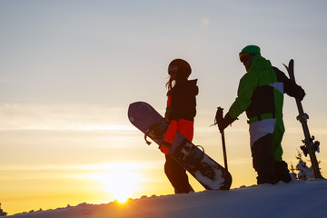 The guy skier and girl snowboarder on the background of the sunset sky. Sheregesh Russia.