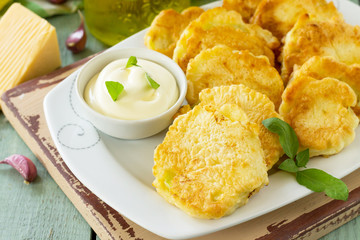 Vegan vegetable fritters zucchini and sour cream garlic sauce on the kitchen wooden table. Fried vegetarian cutlets or pancakes close-up. The concept of fast food.