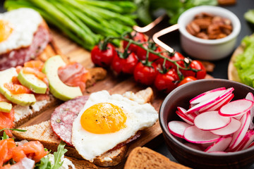 Mediterranean snacks set with brushettas, cheese variety, salami, eggs and salmon over black background on wooden board, top view