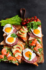 Appetizers table with healthy snacks. Brushetta or sandwich set on the board over black concrete background. Top view, flat lay