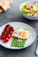 Blanched asparagus, fried egg, tomatoes and sald on the bowl. Breakfast concept