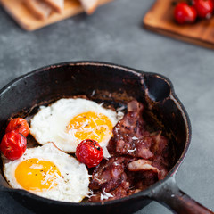 English breakfast of fried egg, tomatoes, bacon and toast on gray background
