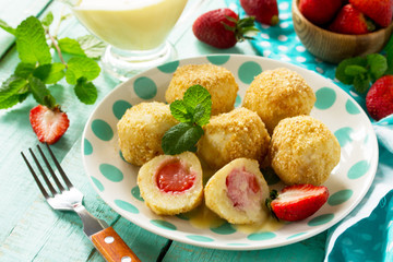 Cottage cheese dumplings with fresh strawberry, served with sour-honey sauce, delicious summer dessert on the kitchen wooden table.