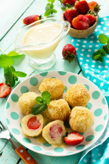 Cottage cheese dumplings with fresh strawberry, served with sour-honey sauce, delicious summer dessert on the kitchen wooden table.