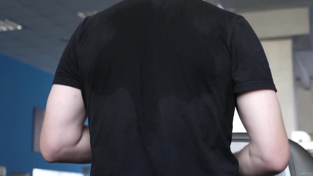 sweaty back men in a T-shirt close-up. fitness club man engaged in walking. strengthening muscles of heart and legs by walking. cardio load. man trains on treadmill. walking in gym. weight loss in gym