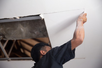 Asian young man using a ladder to repair the broken ceiling at home