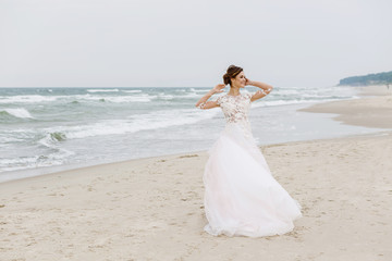 Fototapeta na wymiar Young beautiful bride with a long dress walks on the sea beach