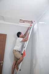 Asian young man using a ladder to repair the broken ceiling at home