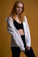 Stylish young girl with curly hair, smiling cutely, posing, on yellow background