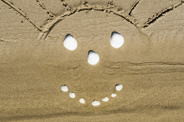 Children's drawing of a smiling sun with shells on the sand on the beach