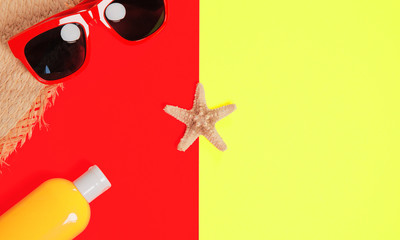 Trendy fashion beach accessories on a bright colorful background. Sunglasses, fragment of a straw hat, a bottle of sunscreen lotion, dried starfish and shells.