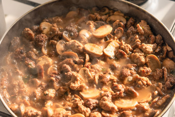 Cooking a stew of homemade sausages and mushrooms in a pan - traditional Italian mushroom sauce Boscaiola.