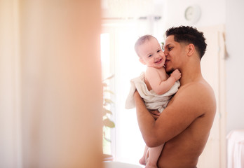 Father and small toddler son wrapped in towel in a bathroom indoors at home.