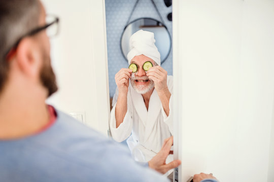 An adult hipster son and senior father in bathroom indoors at home, having fun.