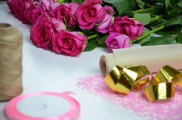 Florist at work: pretty woman making summer bouquet of roses on a working table. Kraft paper, scissors, envelope for congratulations on the table. View from above. Flat lay composition.