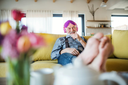 A senior man with headphones and eye mask sitting on sofa indoors at home.