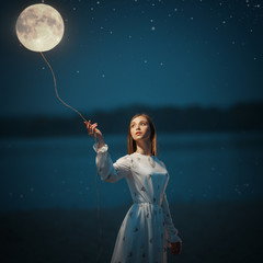 Young attractive girl holds a tied moon on a rope. Art photo.