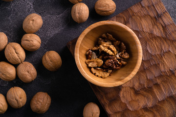 Walnut kernels in wooden bowl and whole walnuts on blue slate surface. Healthy nuts and seeds composition.