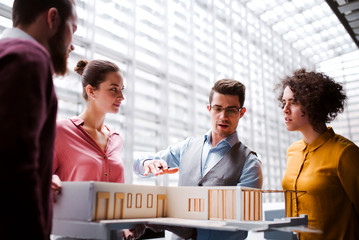 Group of young architects with model of a house standing in office, talking.