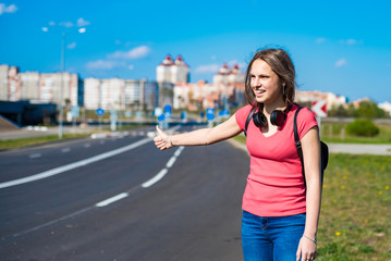 young teenager brunette girl in coral t-shirt with long hair hitchhiking by the roadside. Thumbing a ride. Outdoors vacation.