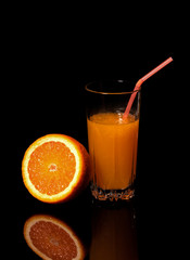 Glass with fresh orange juice and orange on a black background