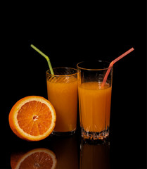 Glass with fresh orange juice and orange on a black background