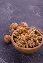 Cracked and whole walnuts in wooden bowl and on blue slate surface. Healthy nuts and seeds composition.
