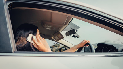 Young woman driving the car and talking on the phone while driving. sun shines through front window. Blurred background and Soft focus.