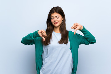 Teenager girl over blue wall showing thumb down