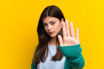 Teenager girl over yellow wall making stop gesture with her hand