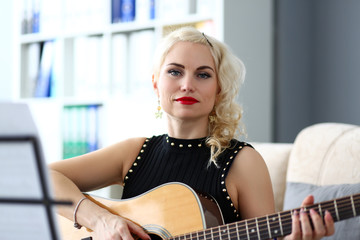 Adult beautiful woman playing acoustic guitar reading notes from stand