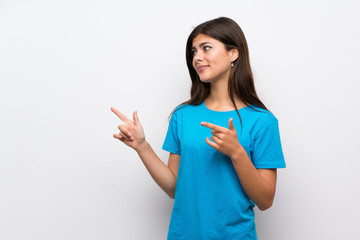 Teenager girl with blue shirt frightened and pointing to the side