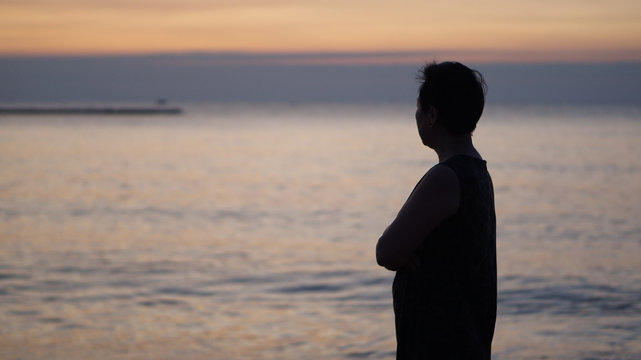 Asian Senior Woman Stand Along Thinking At Sunrise Sea Silhouette