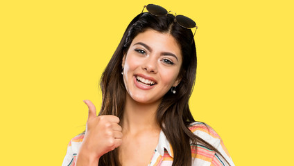 Teenager girl on summer vacation giving a thumbs up gesture over isolated yellow background