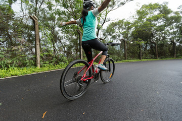 Hands free woman cyclist riding mountain bike on spring forest trail