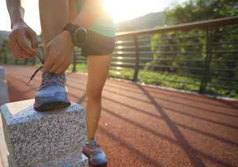 Runner athlete tying shoelace on spring forest trail. woman fitness jogging workout wellness concept.