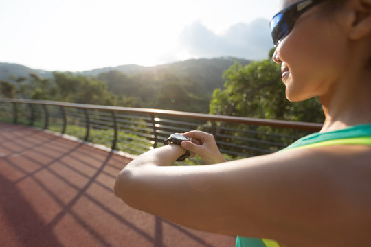 young woman jogger ready to run set and looking at sports smart watch, checking performance or heart rate pulse trace. Sporta and fitness outdoors on forest trail.