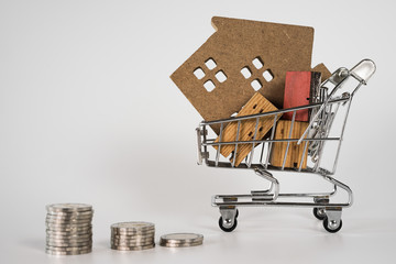 Wood house model in shopping cart and row of coin money on white background. Real Estate market,...