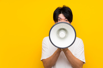 Asian man over isolated yellow wall shouting through a megaphone