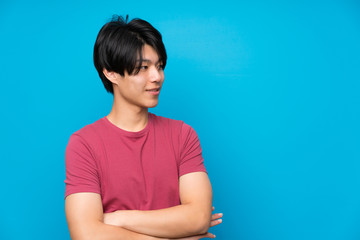 Asian man with red shirt over isolated blue wall standing and looking to the side
