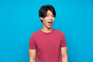 Asian man with red shirt over isolated blue wall with surprise facial expression