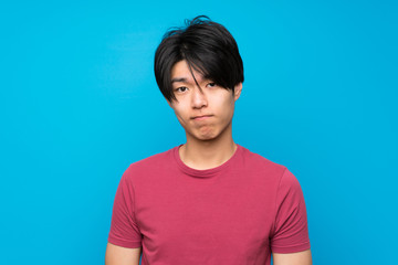 Asian man with red shirt over isolated blue wall sad