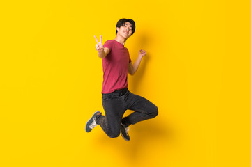 Asian man jumping over isolated yellow wall