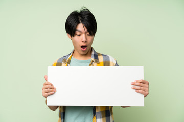 Asian man over isolated green wall holding an empty white placard for insert a concept