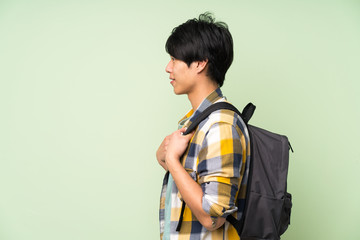 Asian man over isolated green wall with backpack