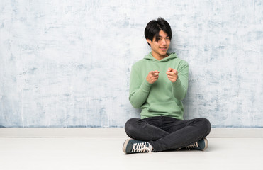 Asian man sitting on the floor pointing to the front and smiling