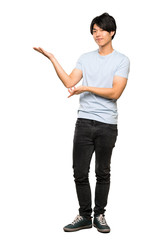 A full-length shot of a Asian man with blue shirt extending hands to the side for inviting to come over isolated white background